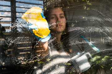 Woman cleaning window glass outdoor with a yellow cloth.
