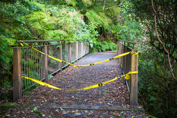 A Department of Conservation hiking track in Milford Sound has 'No Entry' tape across the bridge to signal hazards ahead with a washed out bridge and walkway after severe flooding, New Zealand