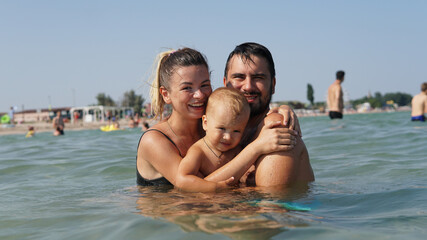 Fototapeta na wymiar Young family hugging in water in sea. Father holding little son in arms