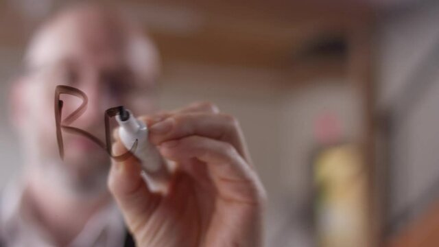 "Reimagine" written on clear plexiglass with a dry erase marker by a modern businessman