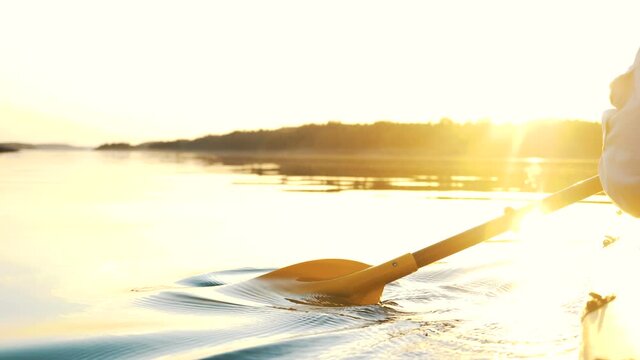 outdoor activities, a man rowing an oar in calm water on a kayak against a golden sunset, camera slow motion