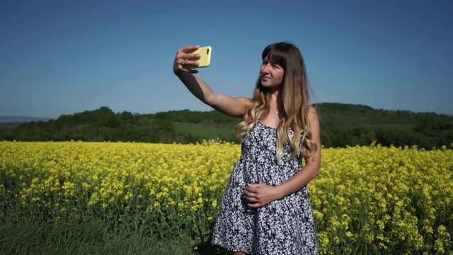 Girl is photographed on a background of rapeseed field, young beautiful girl blogger.Selfie on nature