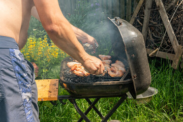A man is putting ready tasty, delicious, savoury meet (chicken wings) from the grill into a plate