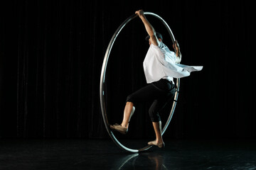 Fototapeta na wymiar Man in circle. Circus performer artist in a Cyr Wheel (Roy Cyr) in theatre at a black background