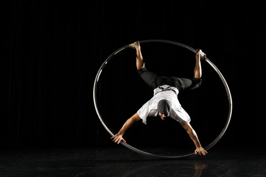 Man in circle. Circus performer artist in a Cyr Wheel (Roy Cyr) in theatre at a black background