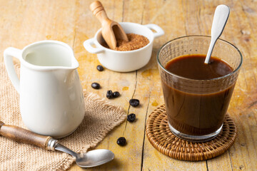 Top view of glass with coffee, coffee beans, brown sugar, milk jug and spoon, with selective focus, on wooden table, horizontal