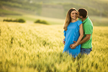 Naklejka na ściany i meble Young husband and his pregnant wife in the summer field