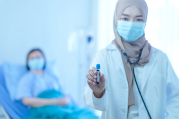 Young muslim female doctor holding test tube with blood for covid-19 analyzing with elderly patient sitting on the bed in hospital