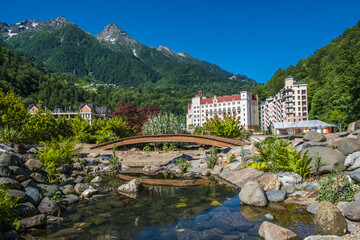 Rosa Khutor. Krasnaya Polyana. Sochi. High mountains. Green trees. Blue sky. Stay. Nature. Panoramic view. Lake. A wooden bridge over the river.