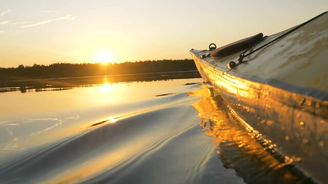 Rubber boat kayak nose cuts the surface of the water at sunset on the lake, outdoor activities