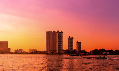Fototapeta na wymiar Dramatic sunset on river with building and boat in Chaophraya river, Bangkok, Thailand