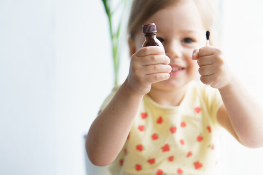 Little Smiling Girl Holding A Medicine Jar Of Iodine And An Ear Stick In Her Hands. Treatment Of Rashes, Acne, Pimples Dermatic Diseases, Contagious Mollusks On Skin In Children. Copy Space.Soft Focus