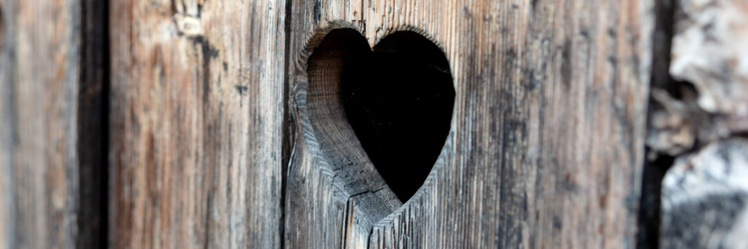 Heart shape at an old wooden door of a toilet. Panoramic image