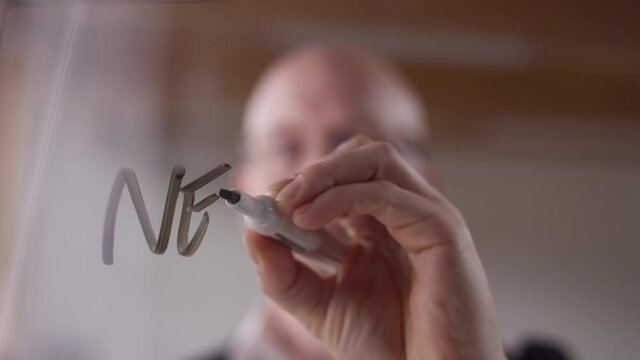 "New Approaches" written on clear plexiglass with a dry erase marker by a modern businessman