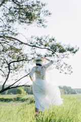 back view of woman in  white dress standing in the meadow with trees 