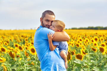 Happy father and son on a summer walk in the field with sunflowers . Father's day
