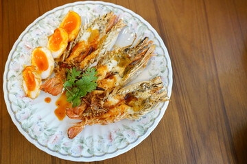 A plate of grilled prawns and fried boiled egg served with sweet and sour tamarind sauce, topped with fried chili and shallot, Traditional thai food.