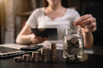 Businesswoman hand puting coins in glass for saving money. concept finance and accounting at home office.