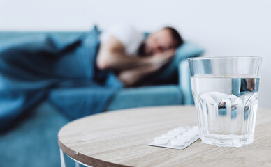 Flu concept. Glass of water with pills on the background of a sleeping sick man