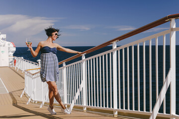 Beautiful lady in striped blue dress on deck of cruise ship with a glass of white wine