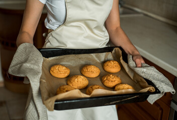 Smiling teen girl taking cookies out of the oven in the kitchen.Homemade cakes, cookies and gingerbread cookies. sweet breakfast
