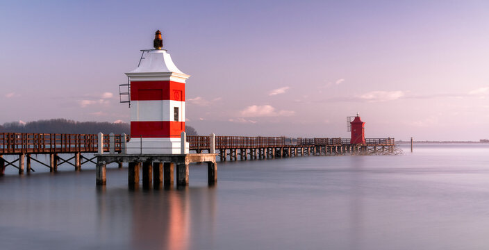 Long exposure shot of the Red Lighthouse of Lignano Sabbiadoro during a cold wintry sunrise. Calm water under a wooden boardwalk. Concept for relax and vacation