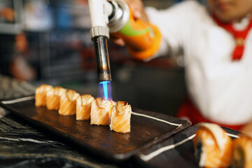Japanese salmon sushi roll, topped with foie gras and Chef using kitchen torch burn on sushi,...