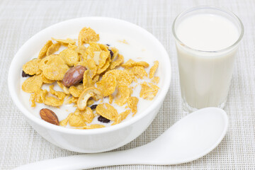 Cornflakes, fresh milk in a white cup with a spoon scooping and a glass of fresh milk on the side