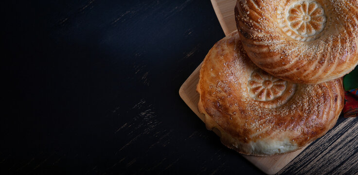 Uzbek tandyr flatbread. Traditional bread in Central Asia - tandyr flatbreadon a black wooden table background, top view, copy space banner.