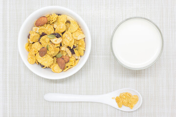 Cornflakes in a white cup and fresh milk in a clear glass and a white spoon placed on the smiling face.