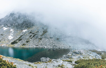 Mountain lake with blue water in the foggy rocky mountains in the rain.