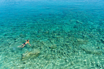 Fototapeta na wymiar A woman swims in blue sea water in the bay. Nature and relaxation, top view