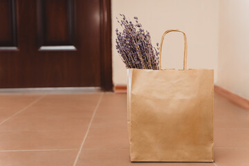 A paper bag with flowers is on the floor in front of the door. Contactless delivery of purchases to...