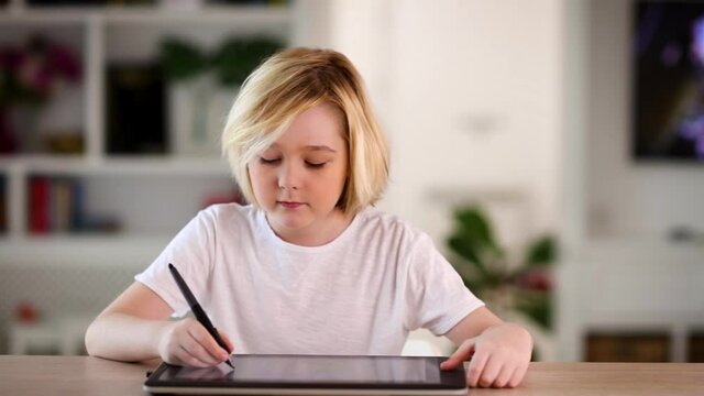 cute blonde kid, boy drawing on the graphics tablet at home