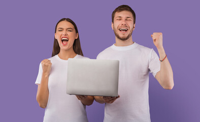 Excited young couple feeling ecstatic holding laptop