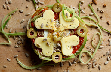 A sandwich with yellow cheese in hearts shape, olives and seeds decoration, flat lay