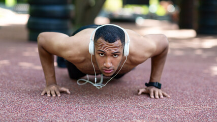 Handsome black man with headphones listening to music and doing push ups on road at park