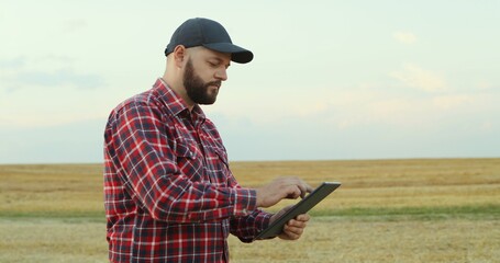 Caucasian farmer man using tablet computer while standing in the middle of his field and looking all around.