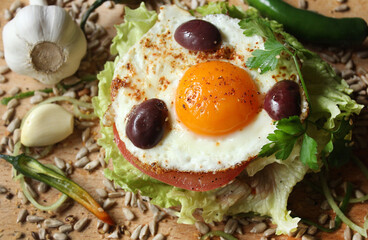 A sandwich with egg, lettuce, tomato, olives and seeds
