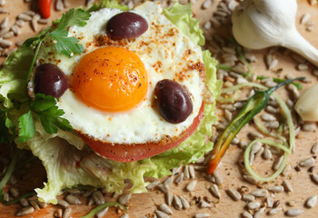A sandwich with egg, lettuce, tomato, olives and seeds