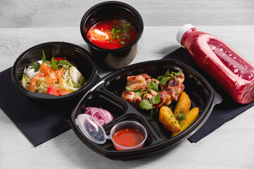 A set of dinner dishes in plastic disposable black dishes on a wooden background. The concept of food delivery.
