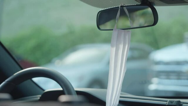 White face mask hanging on car rear view mirror. Traveling with protection concept