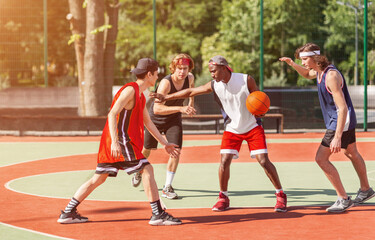 Team of millennial sportsmen engaged in basketball game at outdoor court in summer