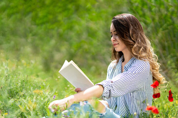 Portrait of woman sitting on lawn in garden reading book