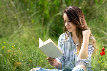 Portrait of woman sitting on lawn in garden reading book