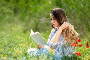 Portrait of woman sitting on lawn in garden reading book