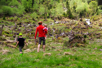 Mother with toddler on arm followed by son exploring the rough country side surrounding the 