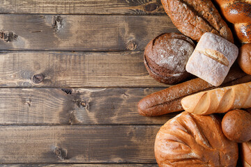 Variety of loaves of bread and buns on wooden table background.