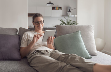 Woman relaxing on the sofa and connecting with her tablet in the living room