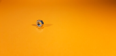 Metalowa, srebrna nakrętka na pomarańczowym tle.